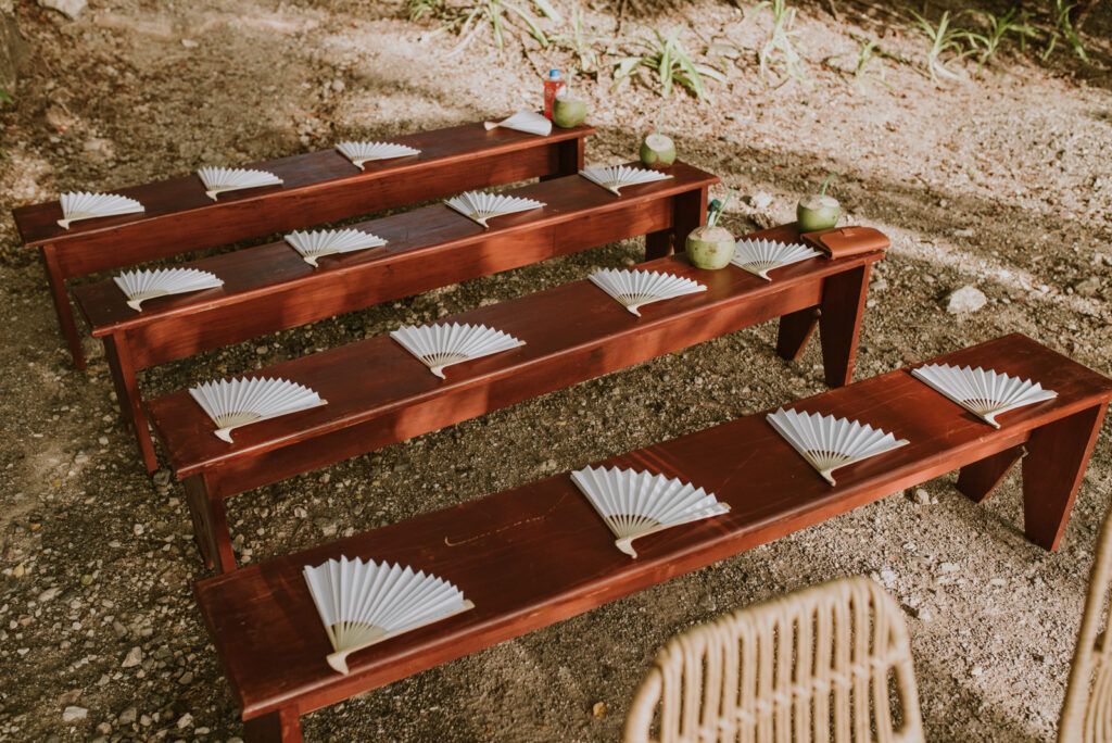 Abanicos blancos colocados sobre bancos de madera para una ceremonia al aire libre