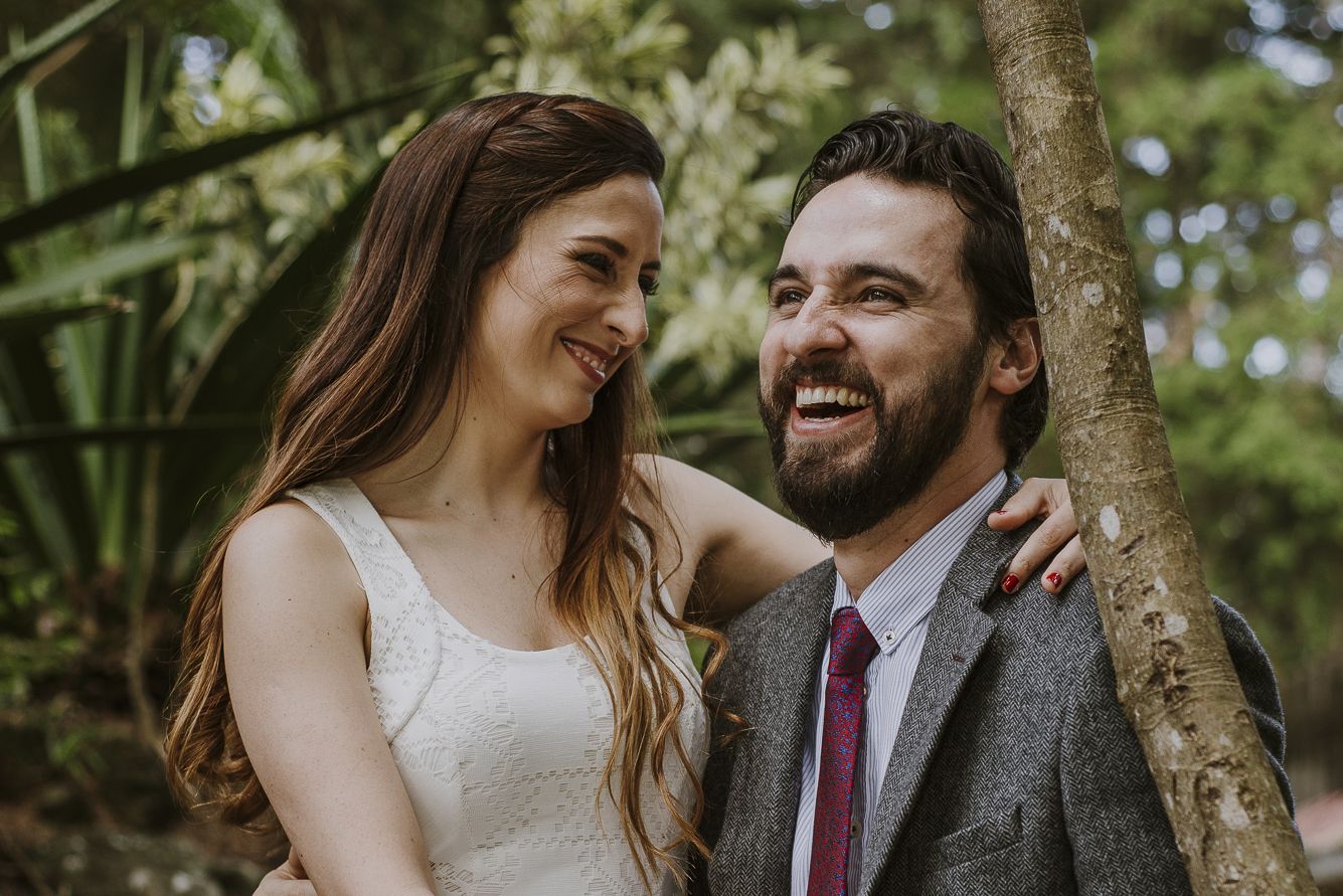 Pareja riendo y abrazada en un jardín durante su sesión de preboda