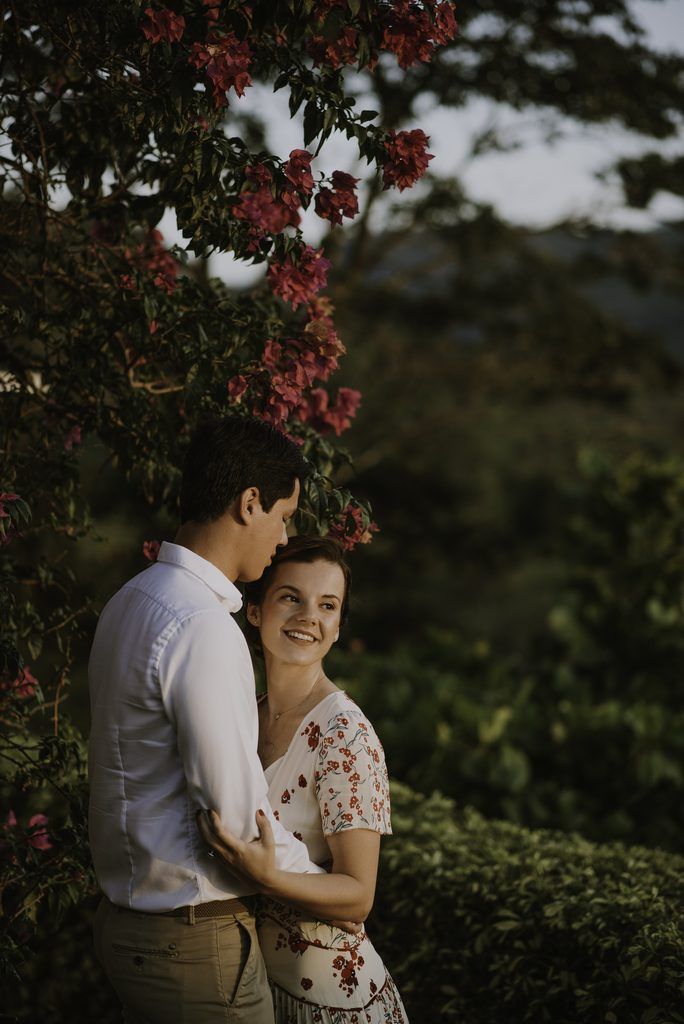 Pareja abrazada bajo unas ramas con flores rojas